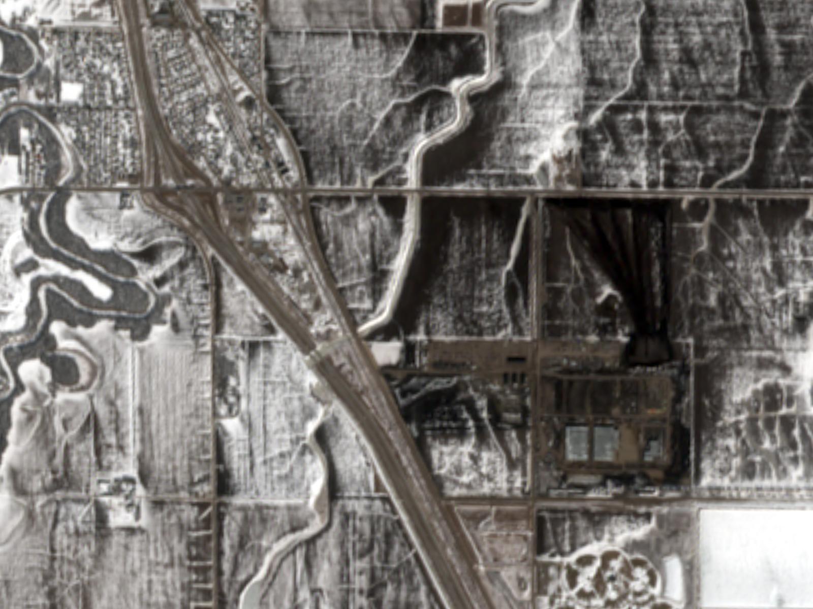 Satellite view of the Polaris Forge 2 construction site in March 2026: the graded campus is a dark rectangle against snow-covered farmland, with Interstate 29 and the town of Harwood to the upper left